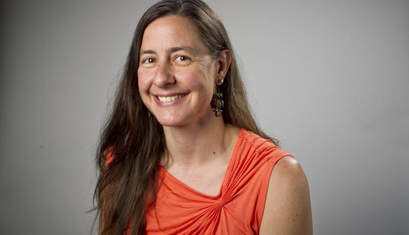 Amy poses in an orange top in front of a gray background