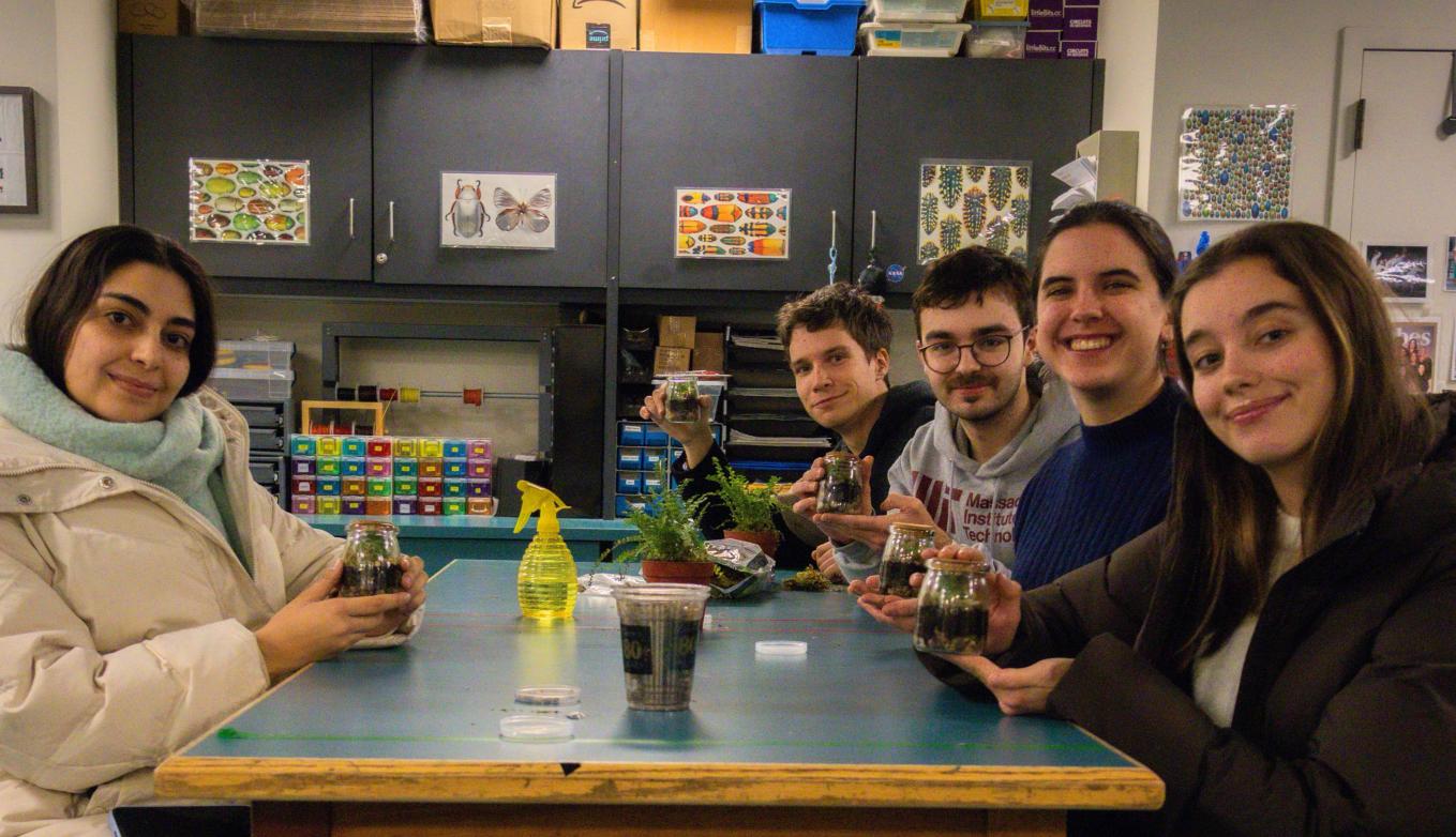 Group of students sits around a class table full of newly-built terrarium jars