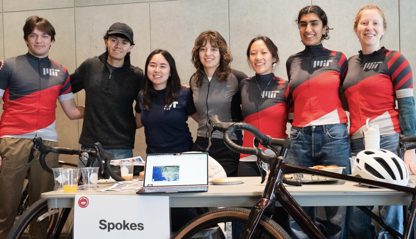 Members of MIT Spokes pose, some in team jerseys, behind their bicycles