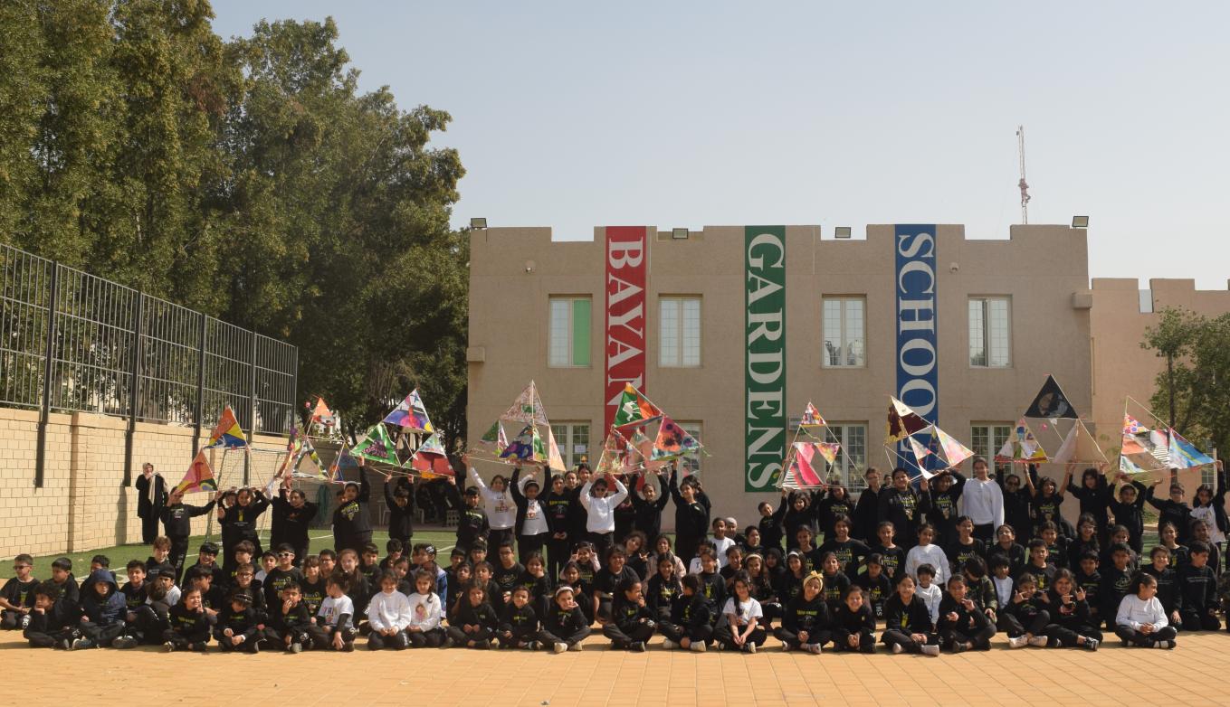 Group of students and MIT visitors smile in front of Bayan Gardens School