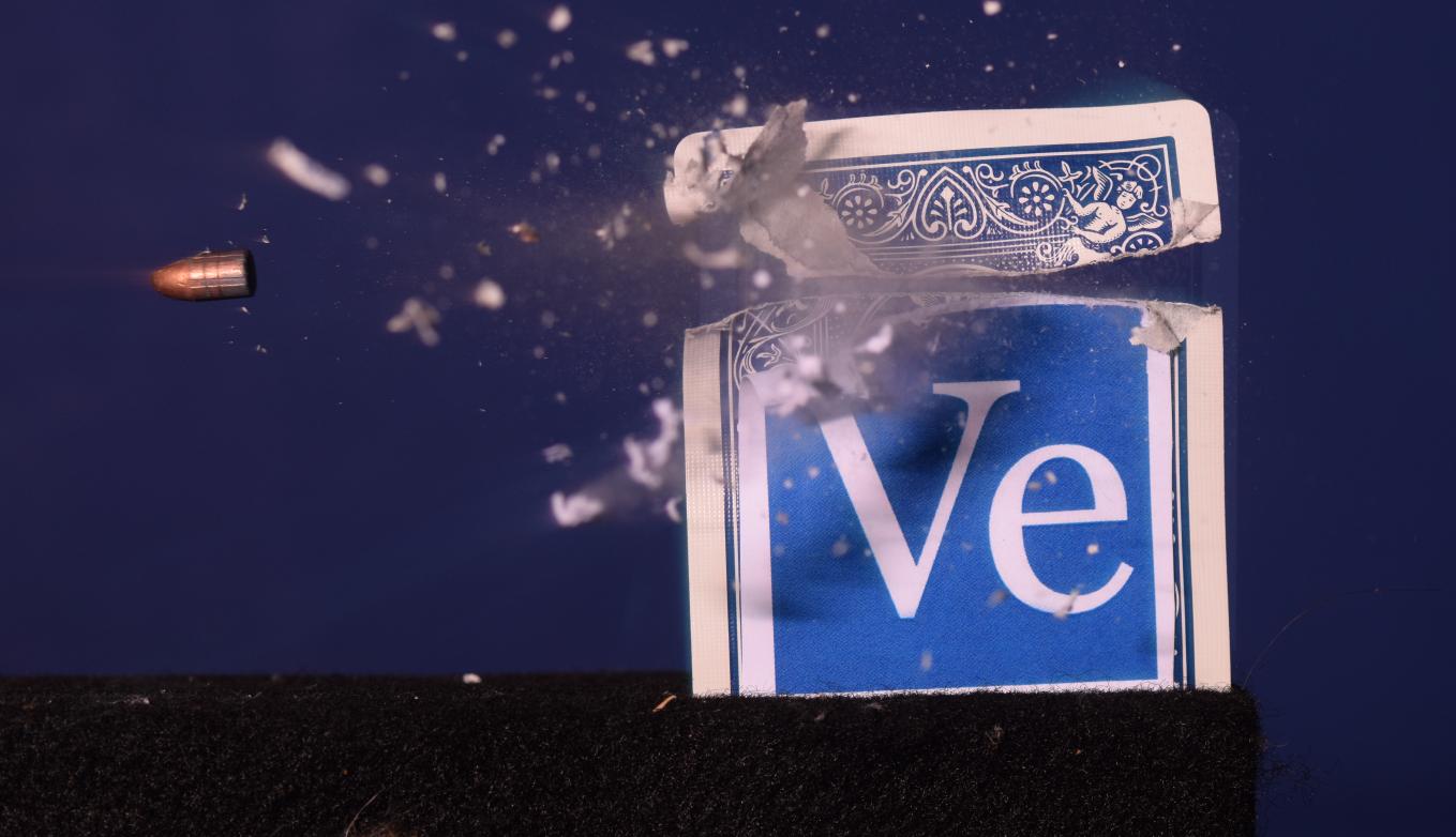 Blue playing card featuring "Ve" Veritasium logo split into two pieces by a bullet, which appears to be frozen midair.