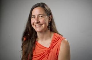 Amy poses in an orange top in front of a gray background