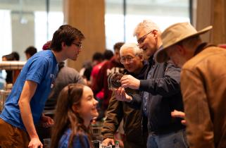 Members of the MIT Wind Team dressed in blue T-shirts chat with visitors, one of whom holds up a component part