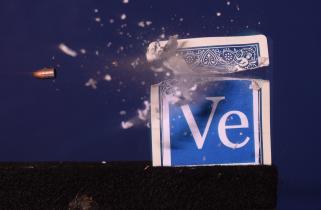 Blue playing card featuring "Ve" Veritasium logo split into two pieces by a bullet, which appears to be frozen midair.
