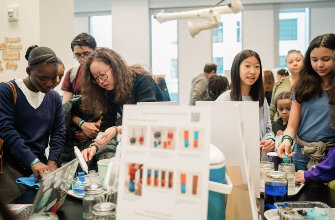 Visitors gather around a table set up with Coastal Climate Change Toolkit posters at the MIT Museum Day of Climate