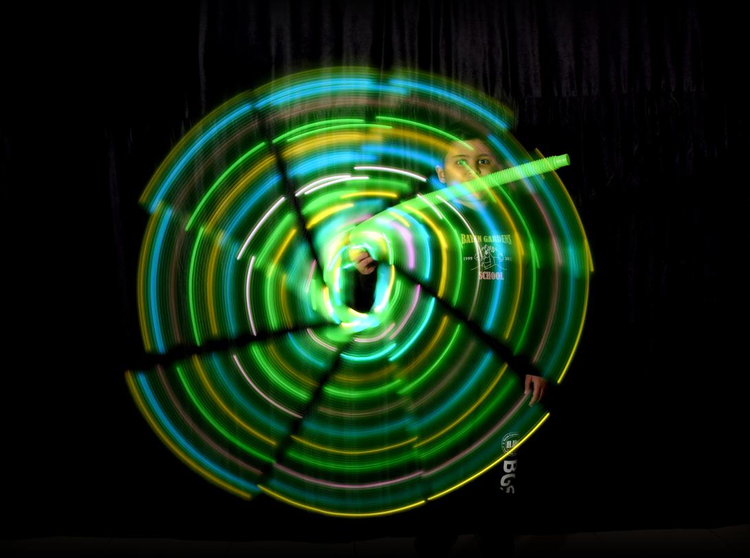 Green and blue lights blur together to create a circle of light in front of a student against a black background